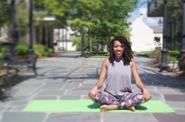 Dr. Valin Jordan sits cross legged on a green yoga mat with her hands at her knees.
